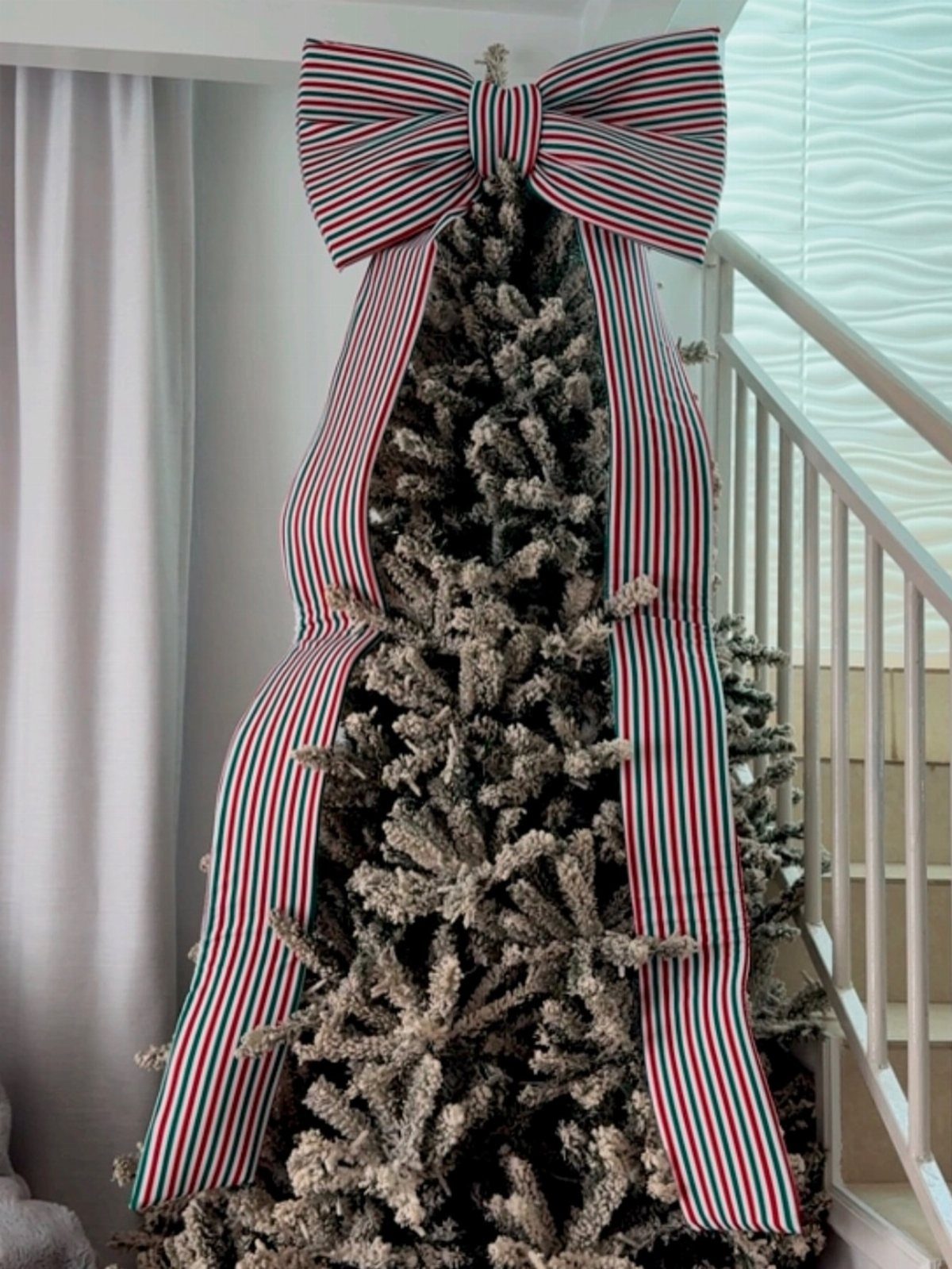 Striped red, white, and green ribbon bow topping a frosted Christmas tree