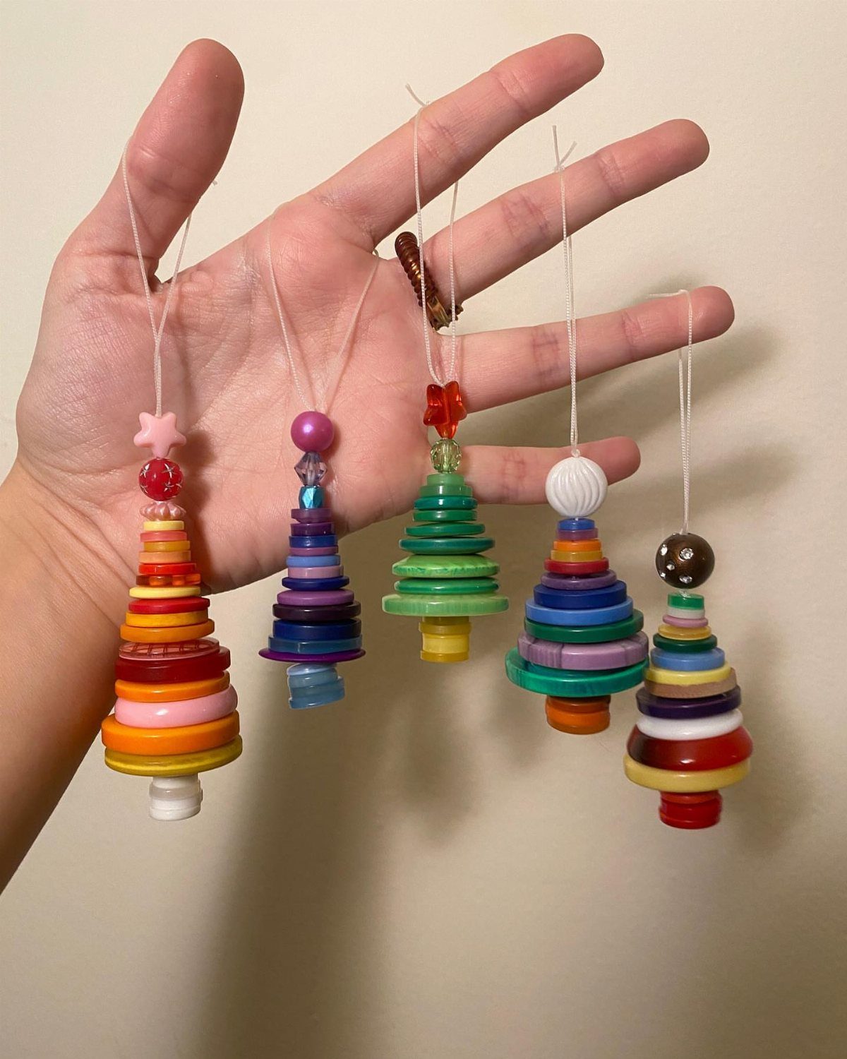 Five colorful button Christmas tree ornaments hanging from a person's open hand.