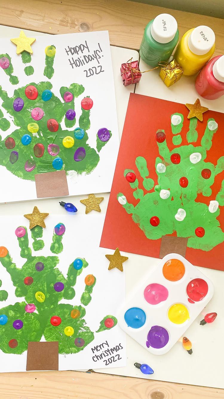 Handprint Christmas tree paintings with colorful dots and gold stars on a table.