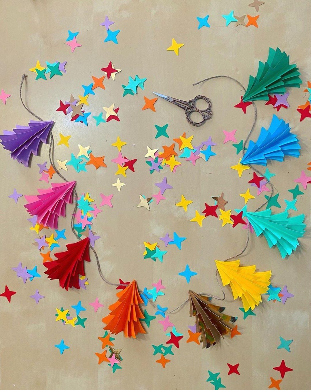Colorful pleated paper Christmas trees strung on a twine garland with paper stars.