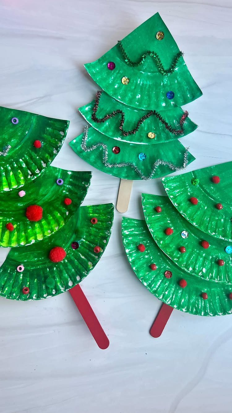Green paper plate Christmas trees decorated with sequins and pom-poms on craft sticks.