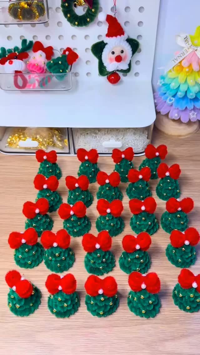 Small green pipe cleaner Christmas trees with red bows on a wooden table.