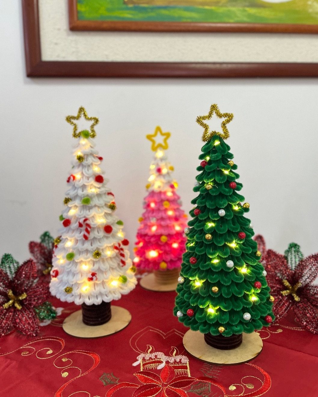 Three small lit decorative Christmas trees in white, pink, and green with gold stars.