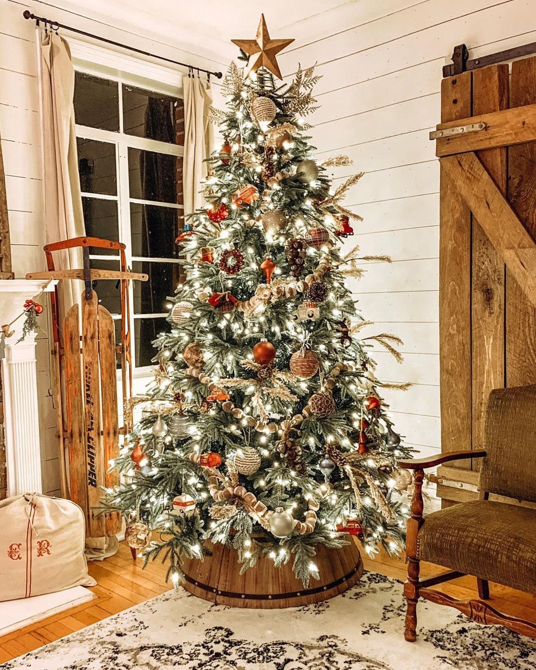 Decorated Christmas tree in a wooden barrel base against white shiplap walls.