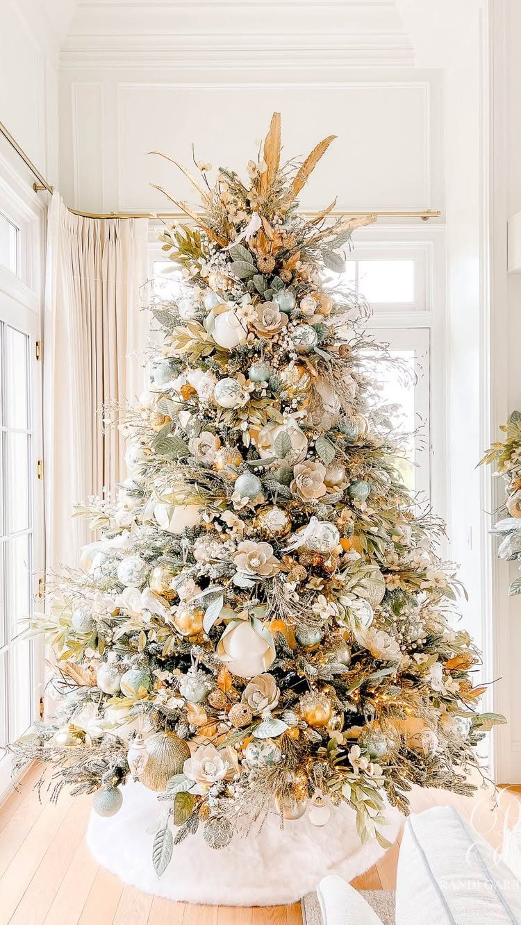 Christmas tree decorated with white flowers, gold foliage, and pale blue ornaments.