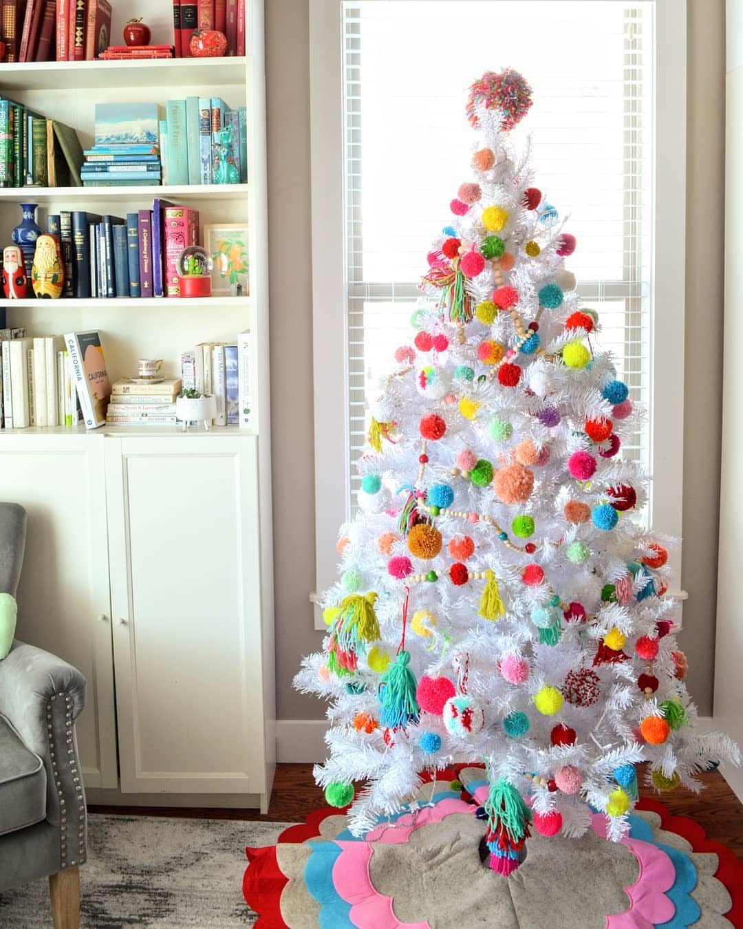 White Christmas tree decorated with colorful pom poms and a pom pom tree topper