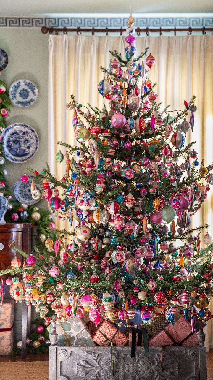 Colorful vintage-style Christmas tree decorated with numerous multi-colored ornaments in a home setting.