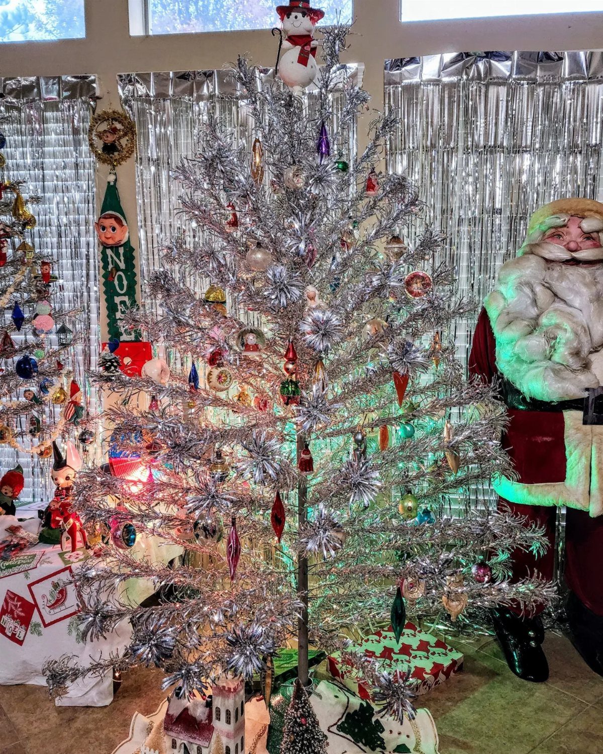 Silver tinsel Christmas tree with colorful ornaments and a snowman tree topper.
