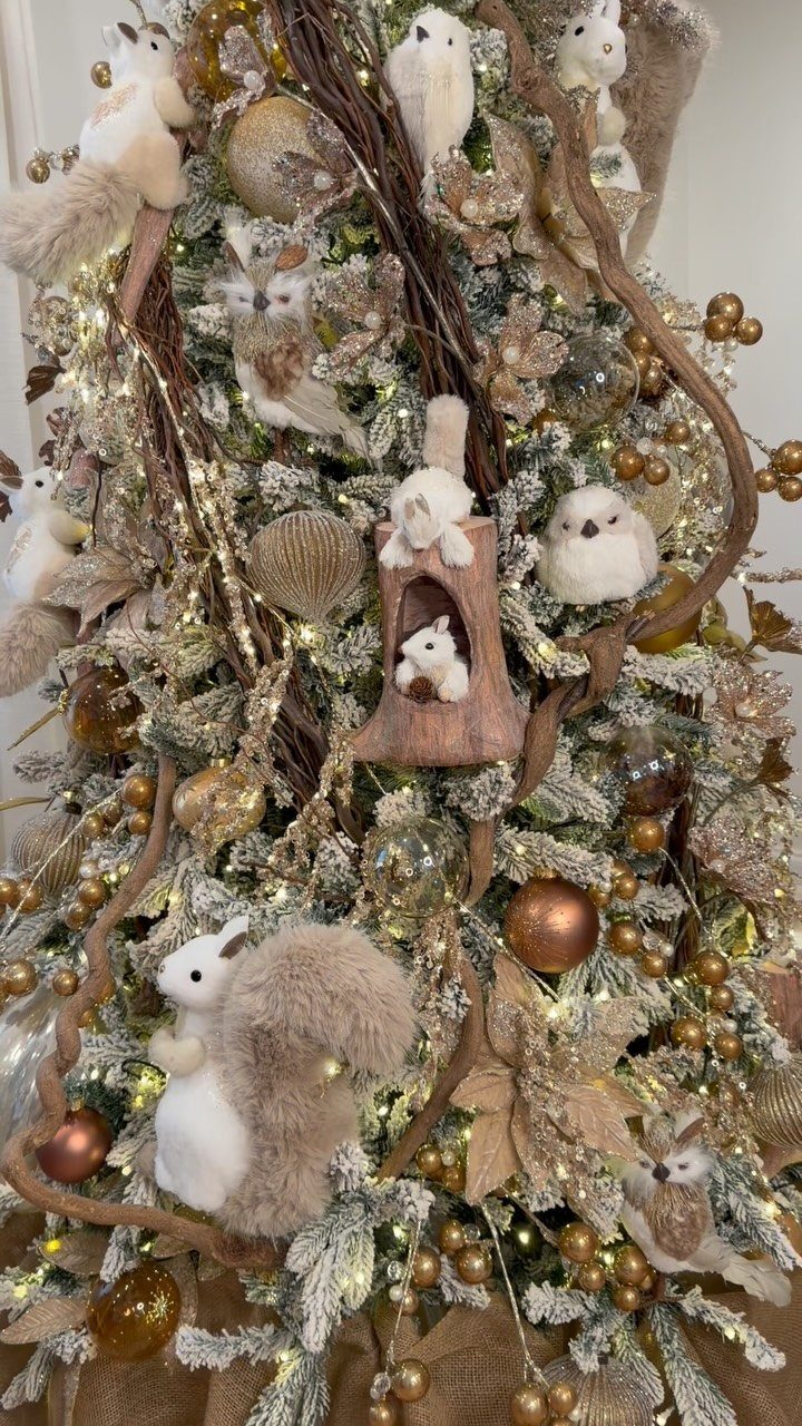 Flocked Christmas tree decorated with plush forest animals, gold ornaments, and wooden twigs.