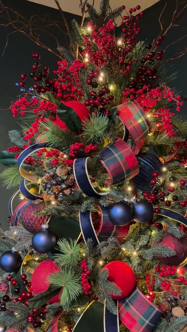 Christmas tree decorated with wide plaid and navy ribbons, red berries, and ornaments.