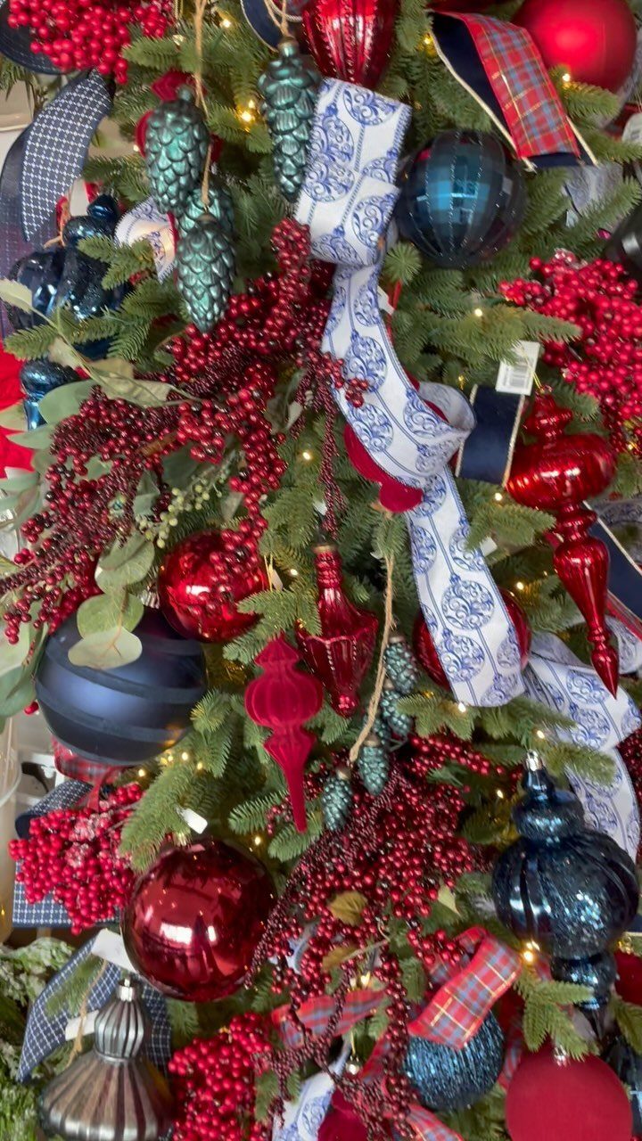 Christmas tree decorated with red and blue ornaments, berries, and mixed material ribbons.