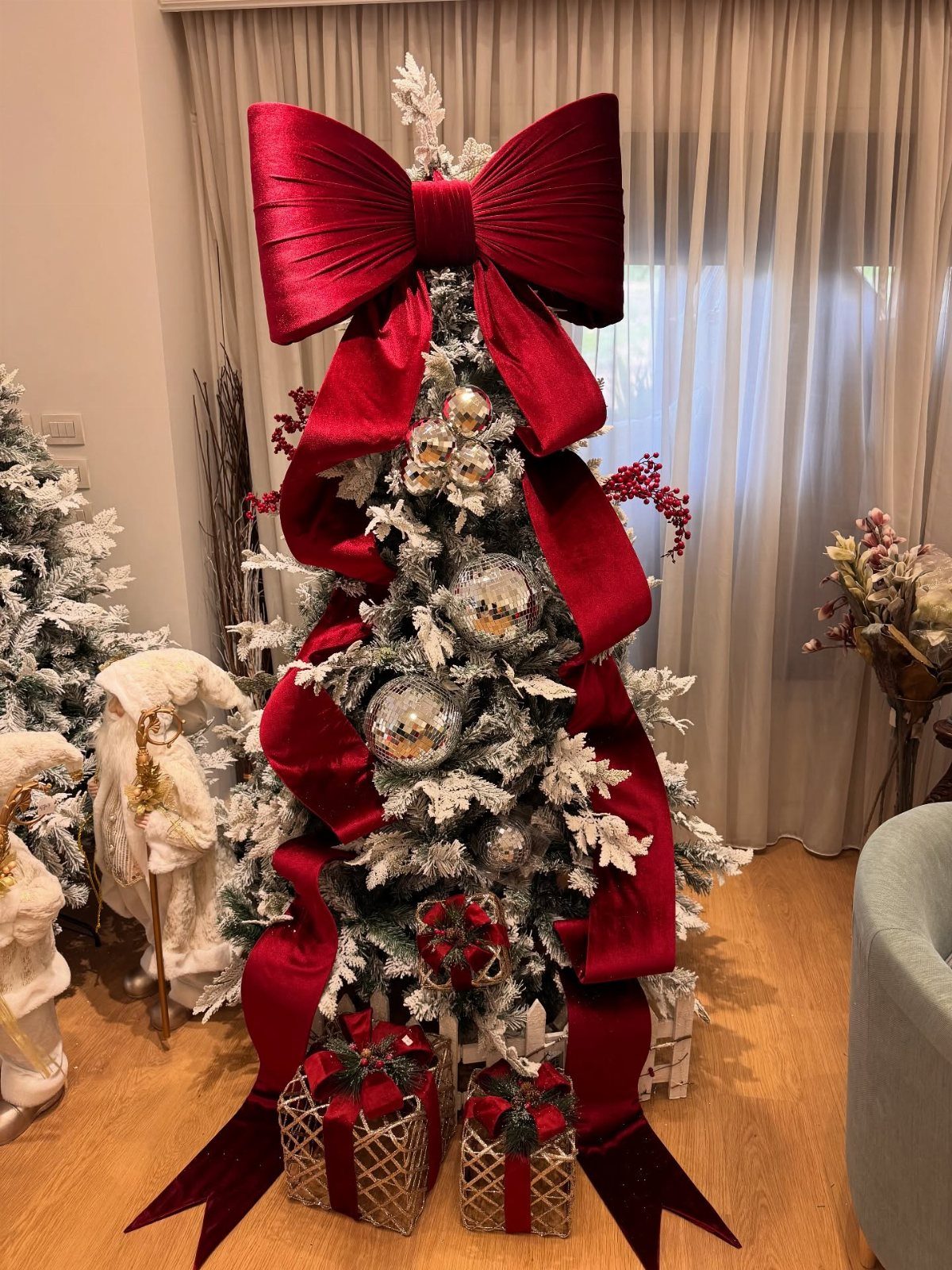 Flocked Christmas tree with a giant red velvet bow topper and cascading ribbon.