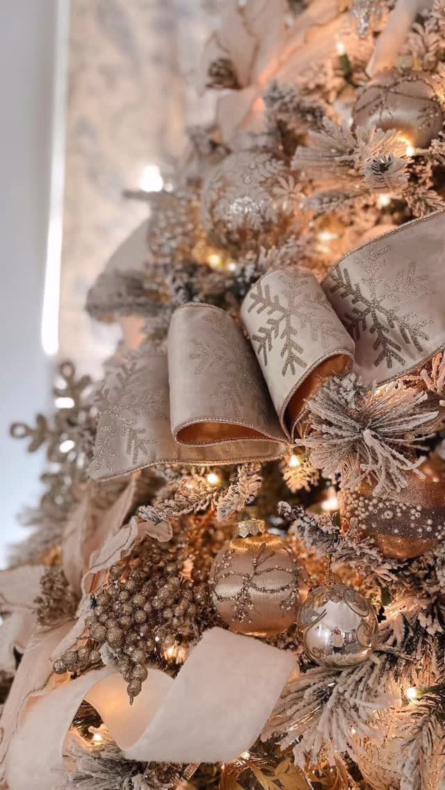 Champagne-colored ribbons and ornaments decorating a flocked white Christmas tree with warm lights.