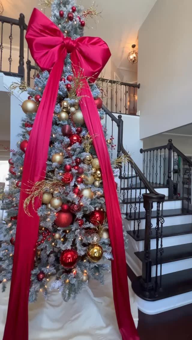 Flocked Christmas tree with red and gold ornaments and a large red statement ribbon.