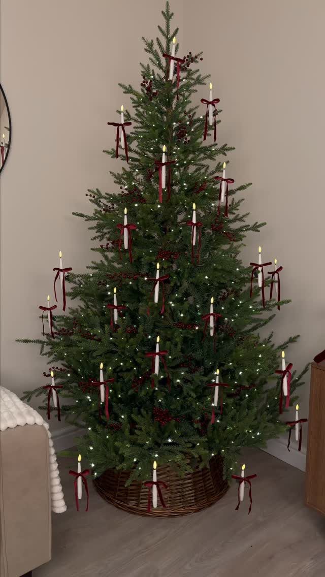 Christmas tree decorated with white candles tied with red ribbons in a wicker basket