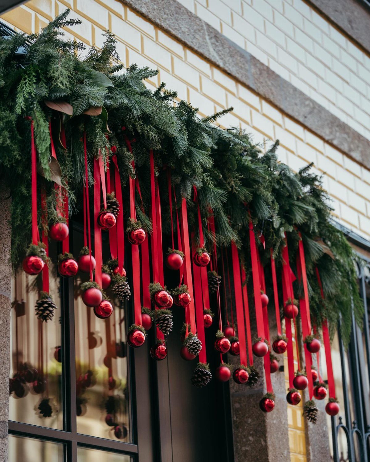 Evergreen garland draped over a window with red ribbons, baubles, and pinecones.