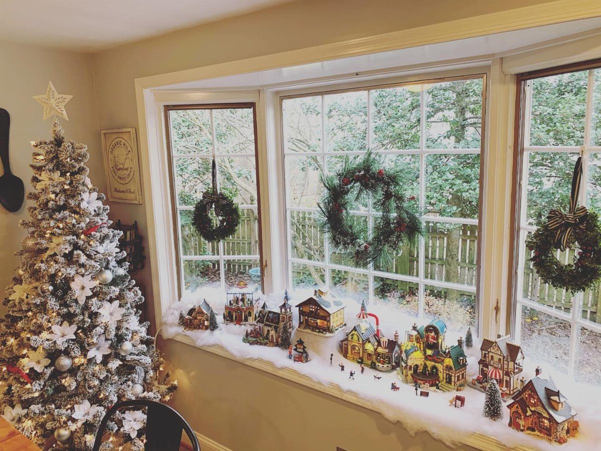 Miniature Christmas village with small houses on a snowy window sill with wreaths.