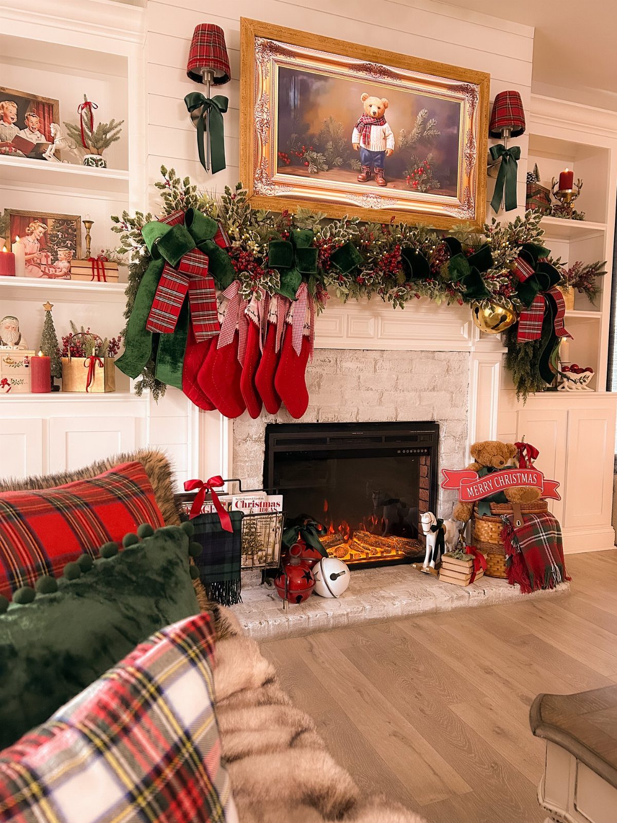 Plaid red and green pillows on a sofa in front of a decorated fireplace.