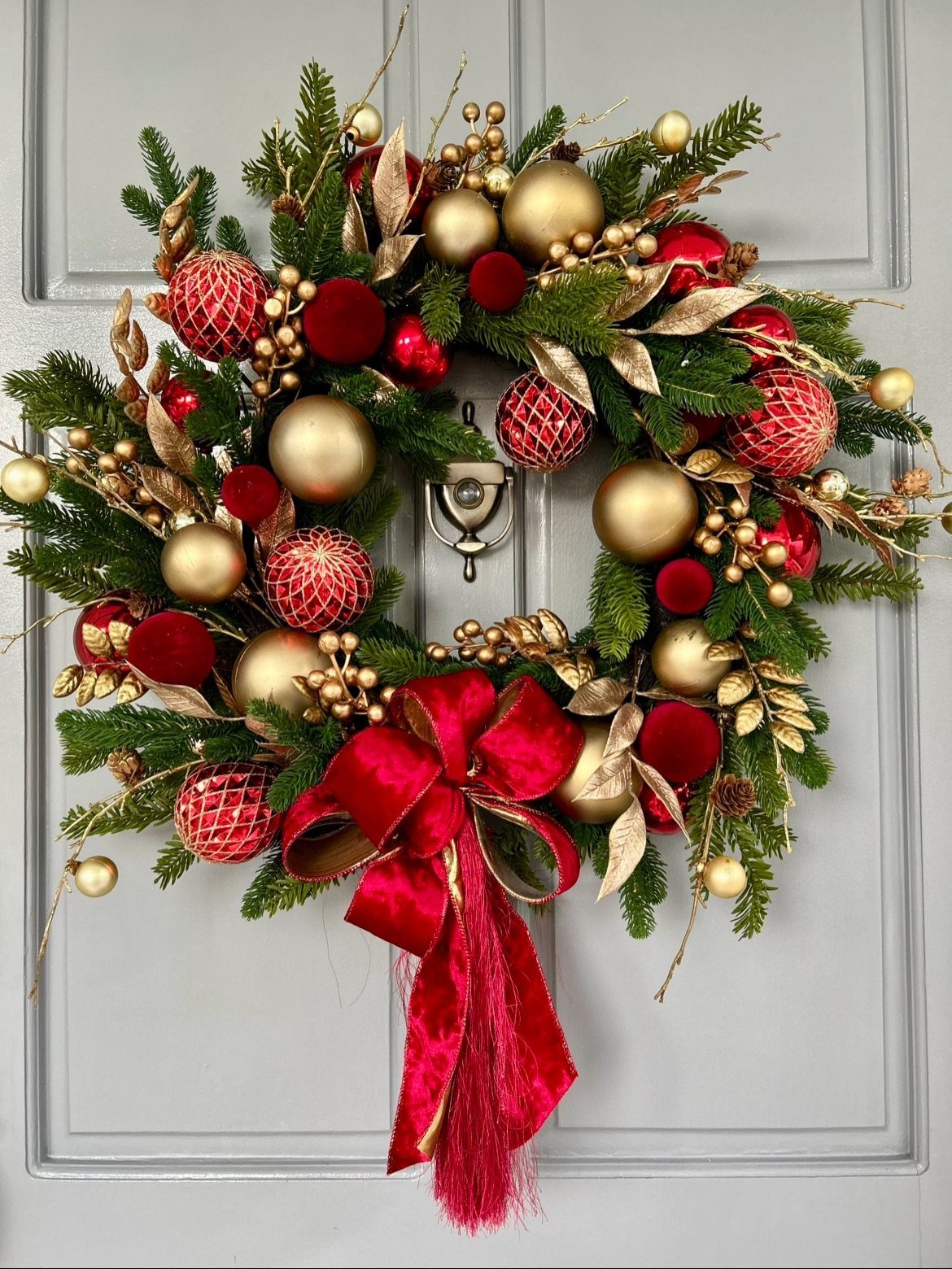 Evergreen wreath with red and gold ornaments and a red velvet bow on a door