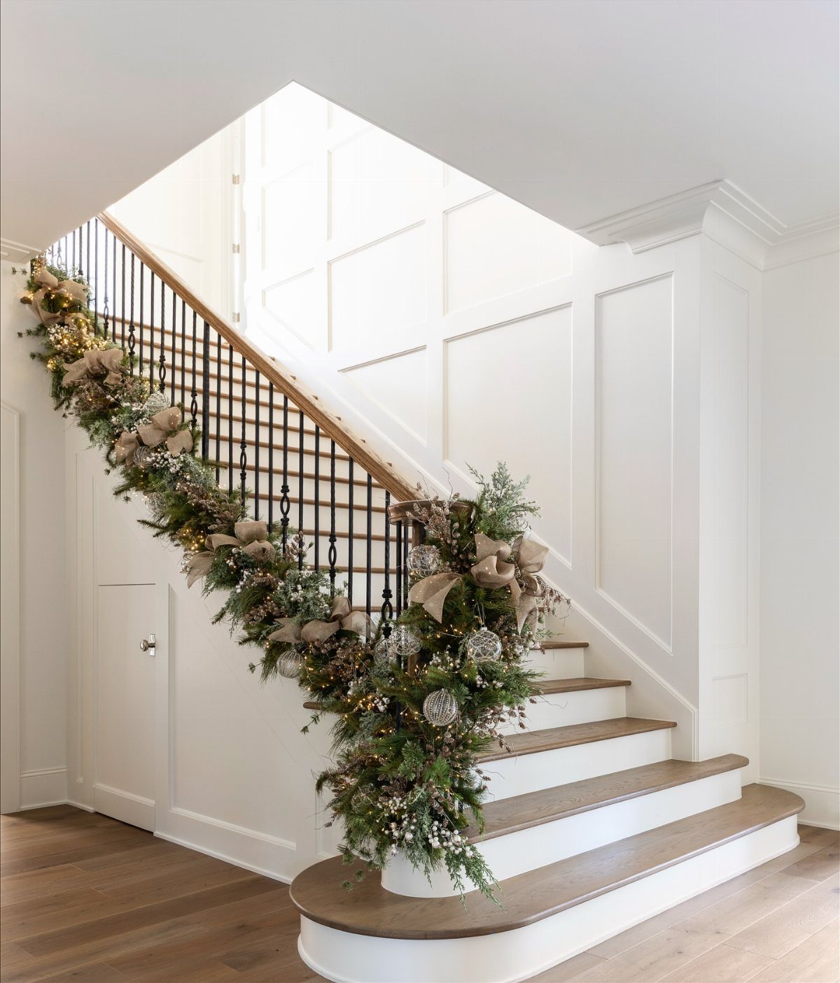Evergreen garland with gold ornaments and bows draped on a white staircase railing.
