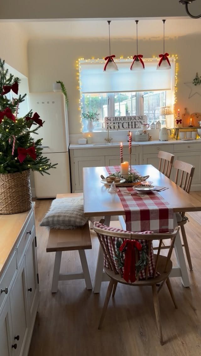 Wooden dining table with red checkered runner and candles in a festive kitchen.