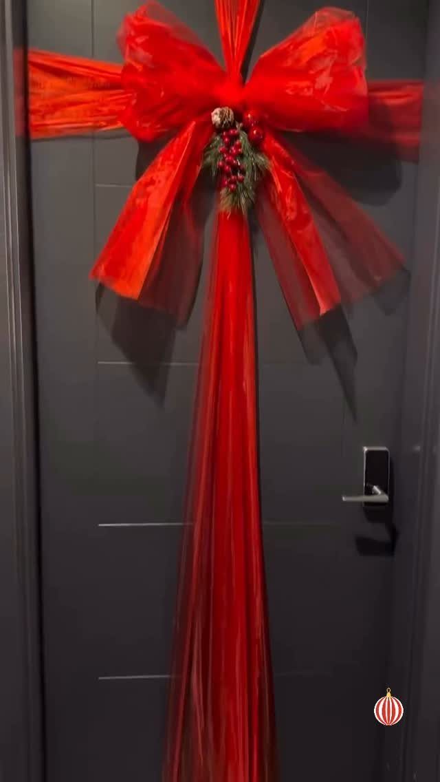 Large red sheer ribbon bow with greenery decorating a dark grey door.