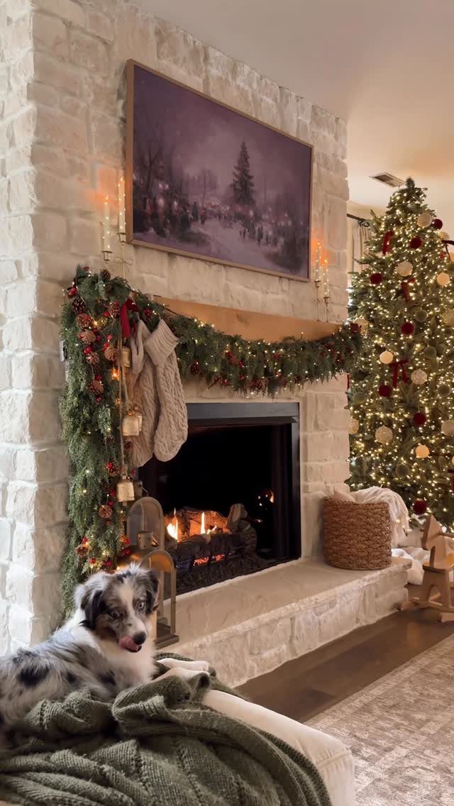 Green pine garland with red ornaments draped over a white stone fireplace mantel.
