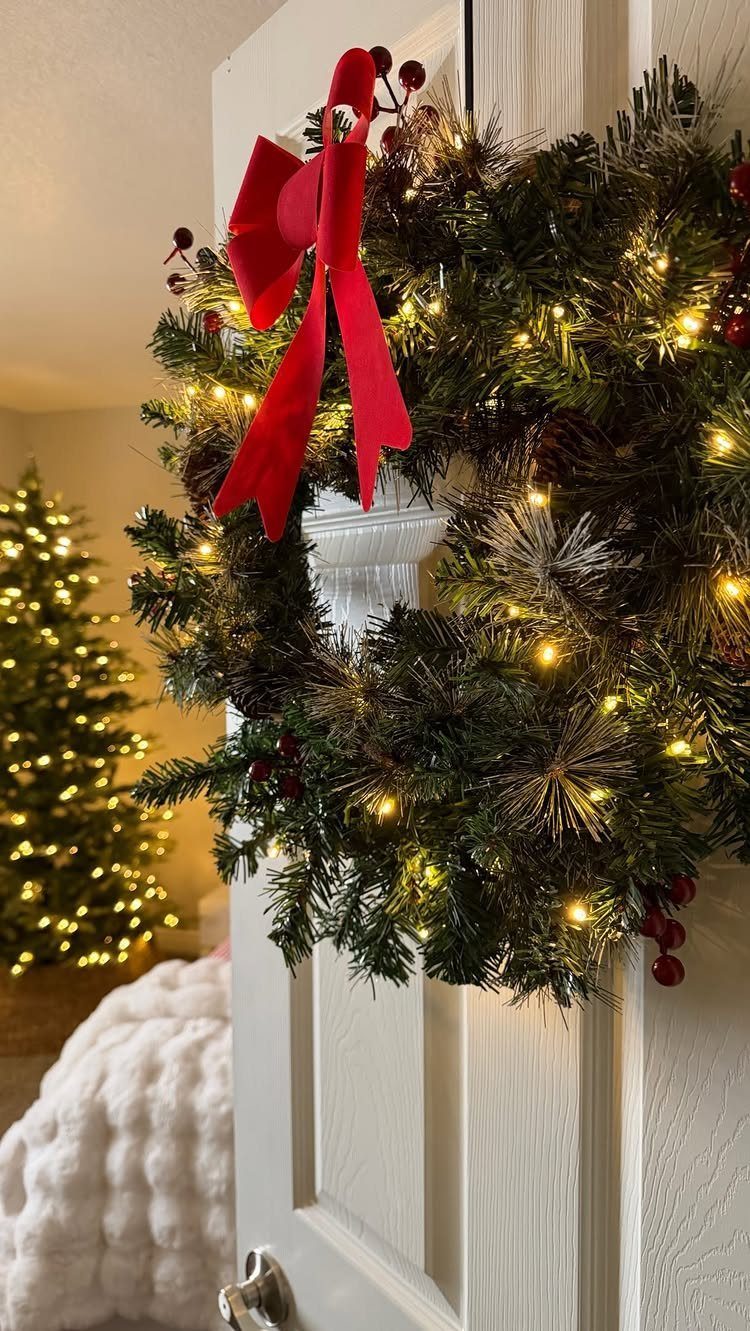 Evergreen wreath with red bow and lights hanging on a white interior door