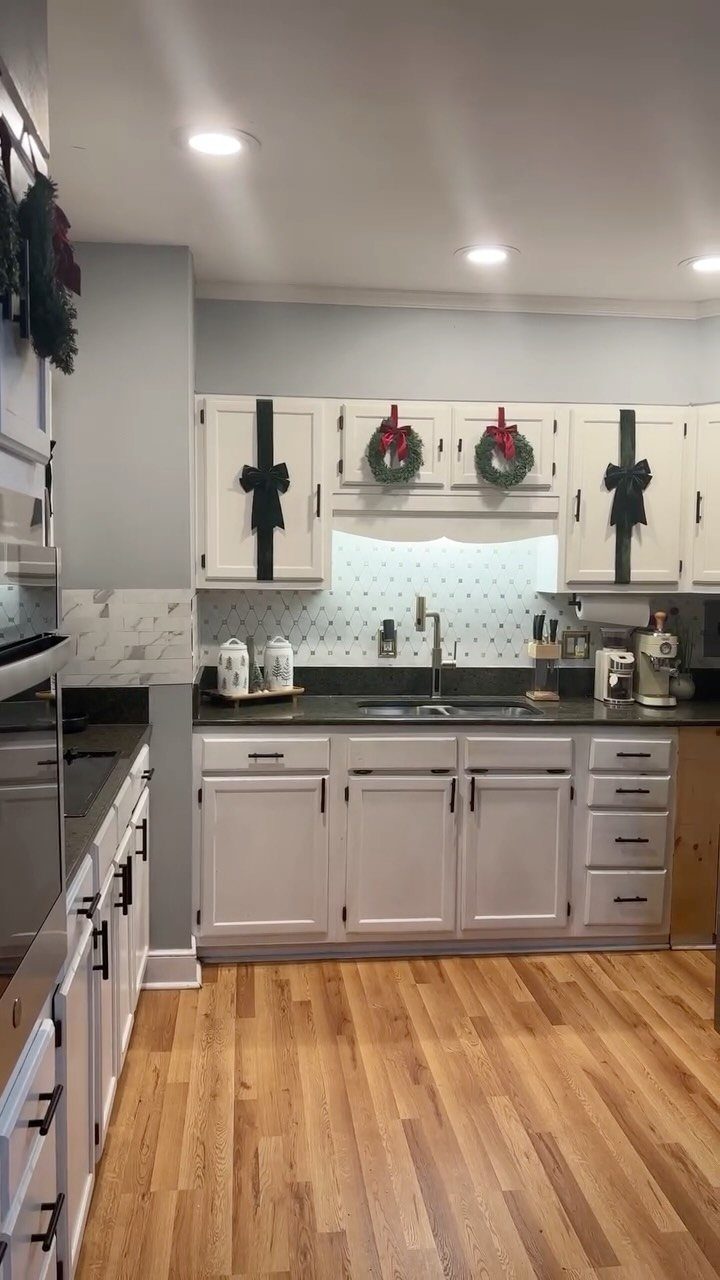 Mini green wreaths with red bows hanging on white kitchen cabinet doors.