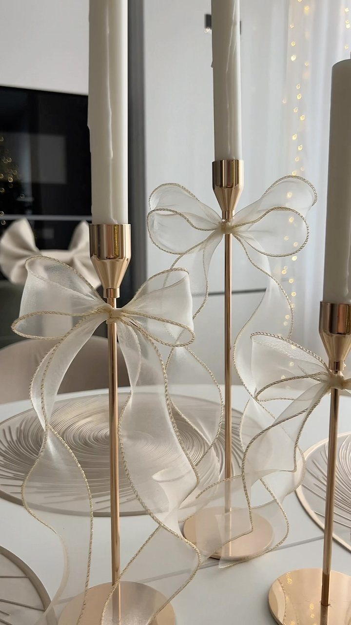 Gold candle holders with white taper candles and sheer white bows on a table
