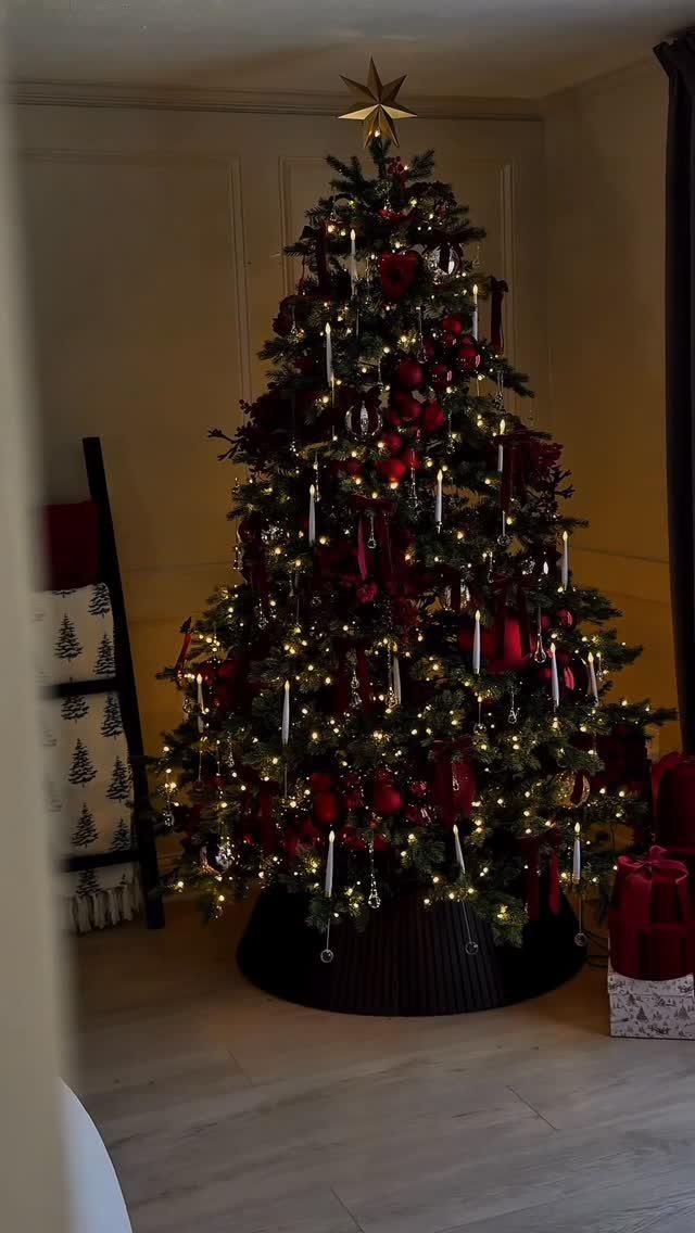 Decorated Christmas tree with red ornaments, warm lights, and white candle-shaped ornaments.
