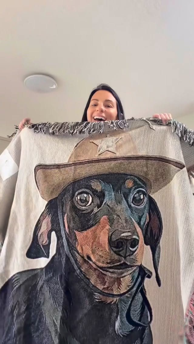 Woman holding a woven blanket featuring a dachshund wearing a cowboy hat