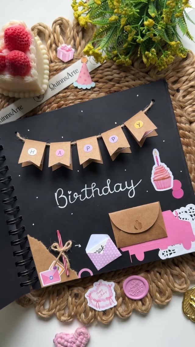 Black spiral notebook decorated with a birthday banner and small paper envelopes.