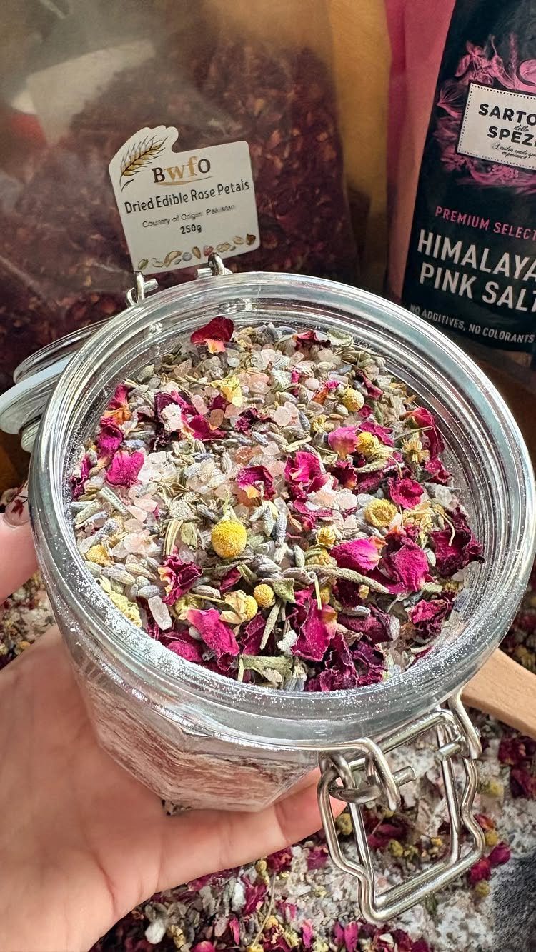 Glass jar filled with bath salts and dried flower petals held by a hand.