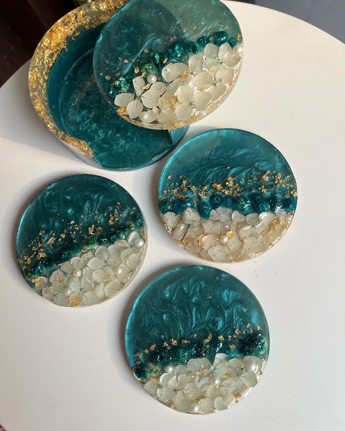 Circular resin coasters with teal swirls, gold flakes, and white decorative pebbles.