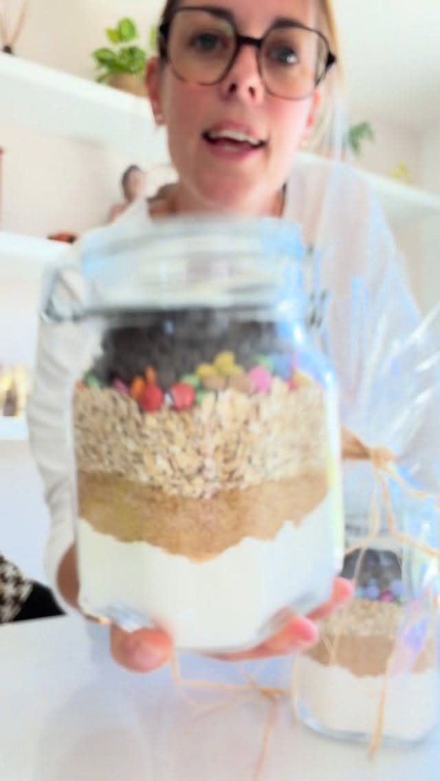Glass jar filled with layered cookie mix ingredients held by a woman.