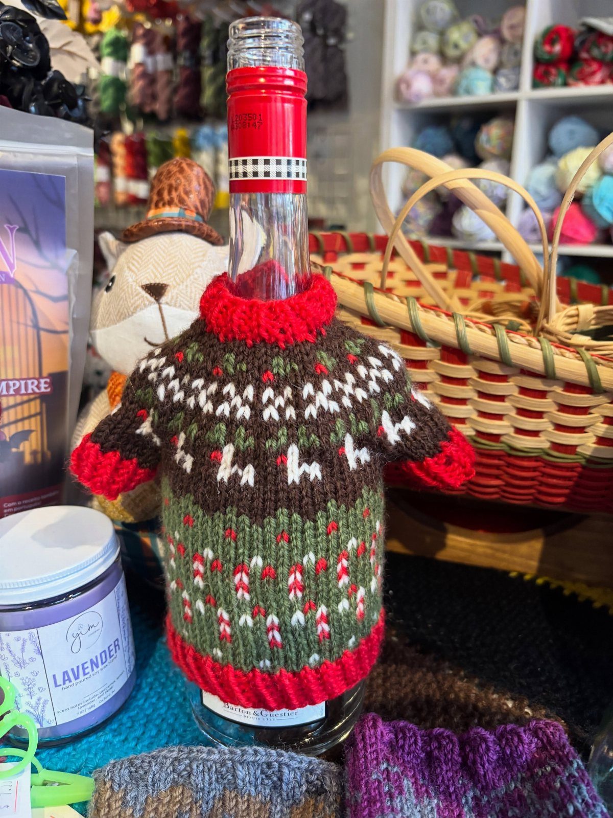 Wine bottle wearing a knitted fair isle sweater with red trim and reindeer patterns.