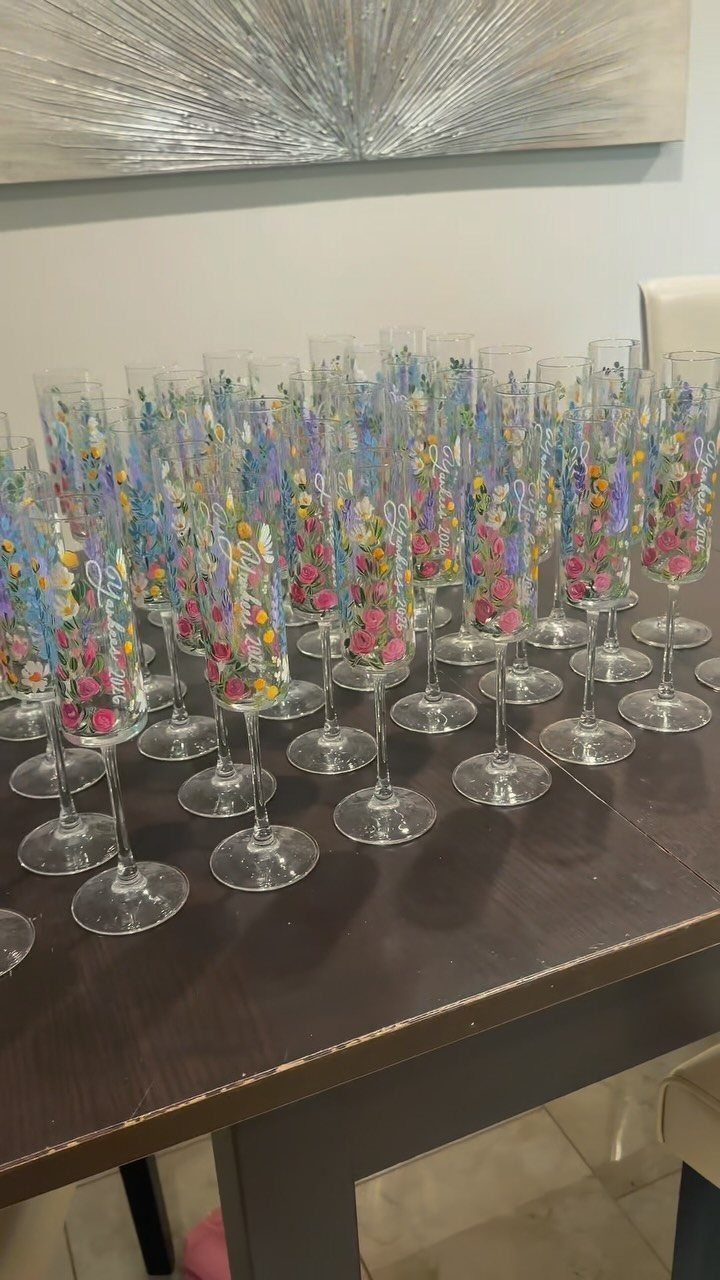 Hand-painted champagne flutes with colorful floral designs arranged on a dark wooden table.