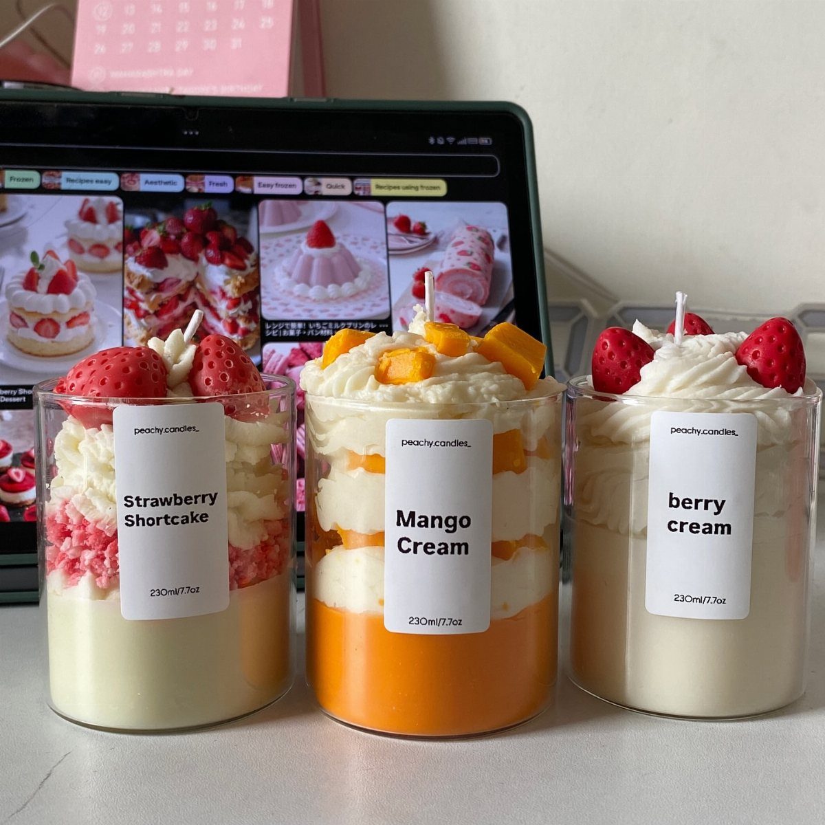 Three dessert-themed candles in glass jars with whipped wax and fruit toppings.