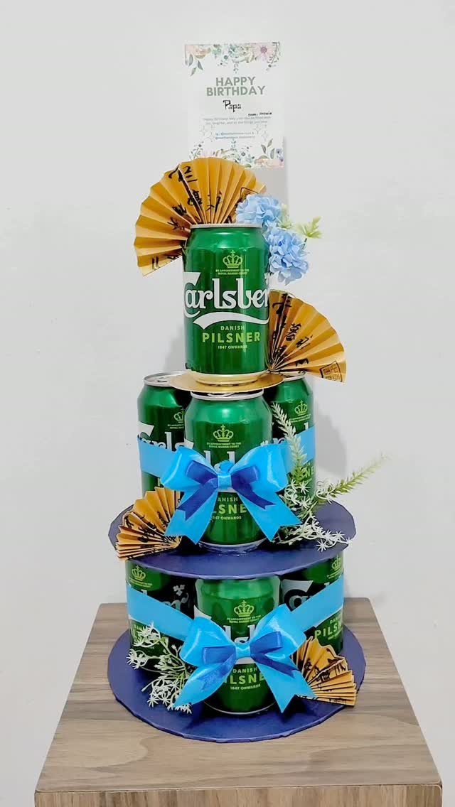 Beer can cake decorated with blue ribbons and gold fans for a birthday gift
