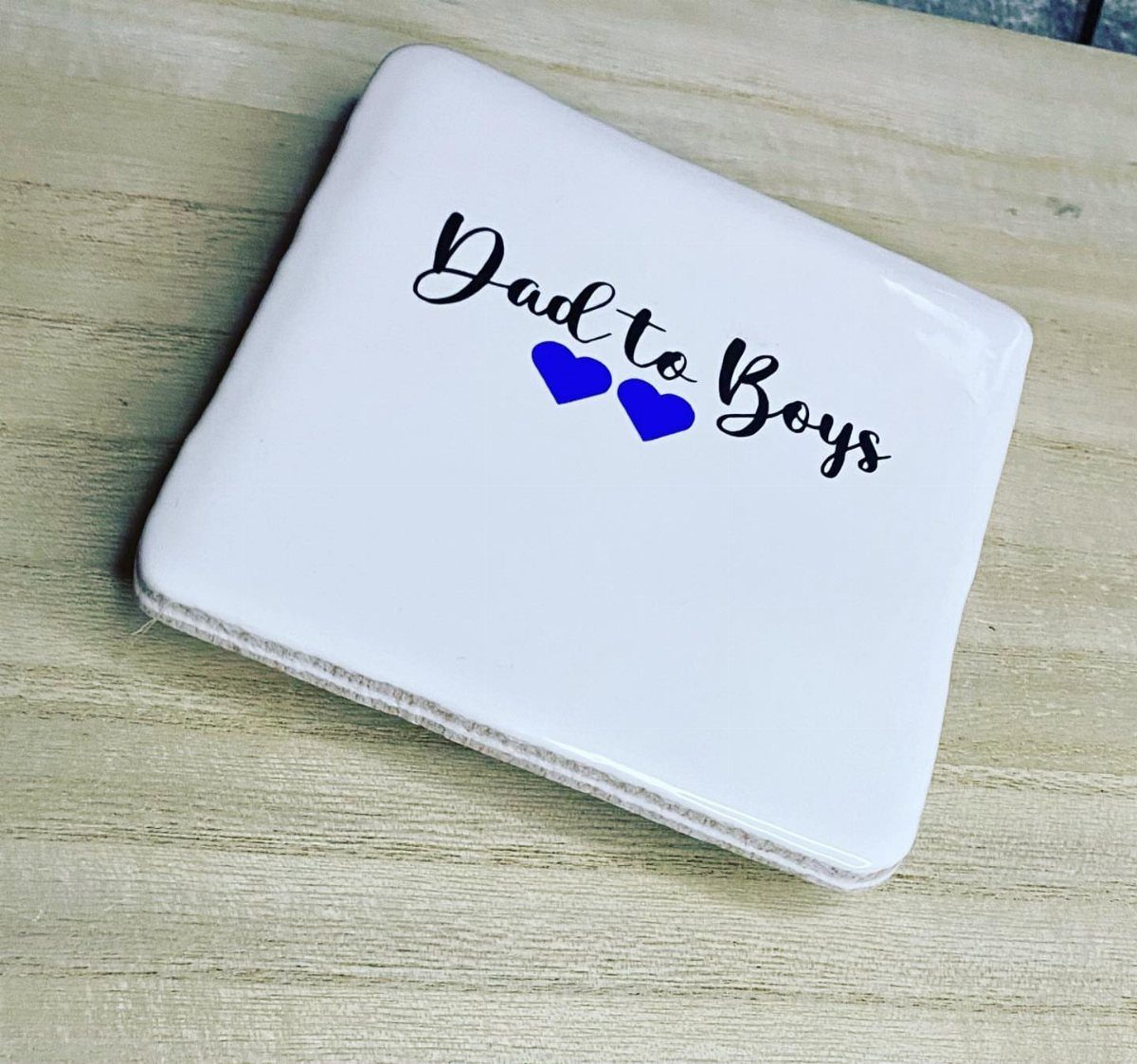 White ceramic coaster with 'Dad to Boys' text and blue hearts on wood.