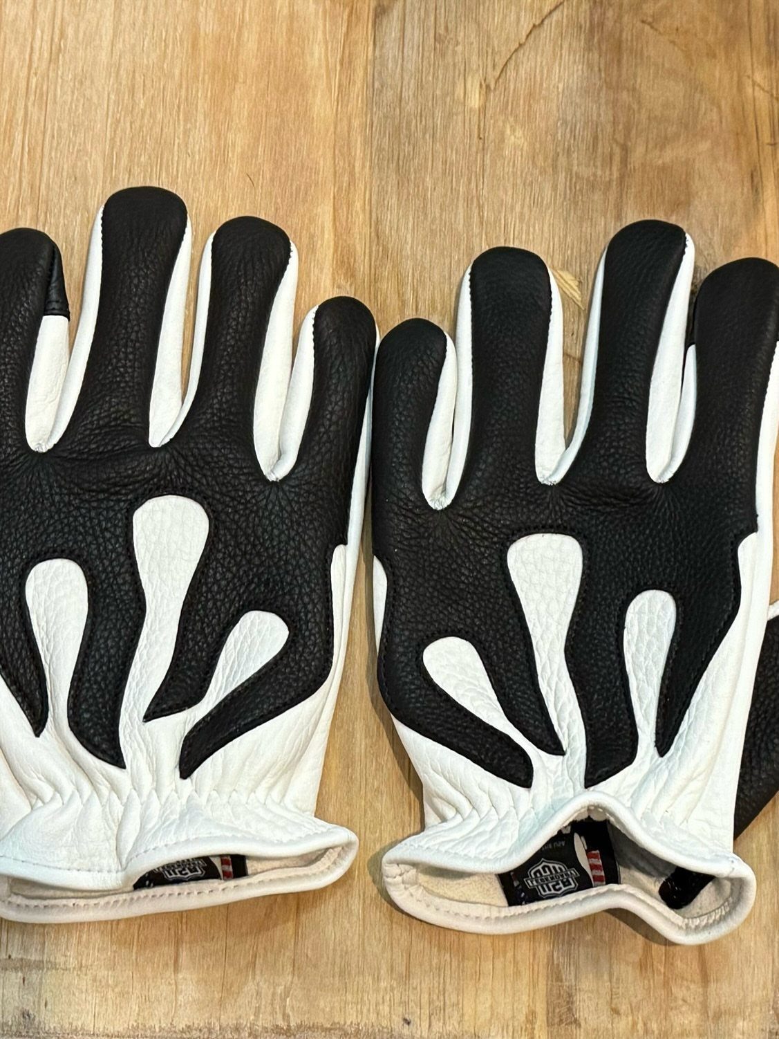 Black and white leather motorcycle gloves with flame patterns on a wooden background