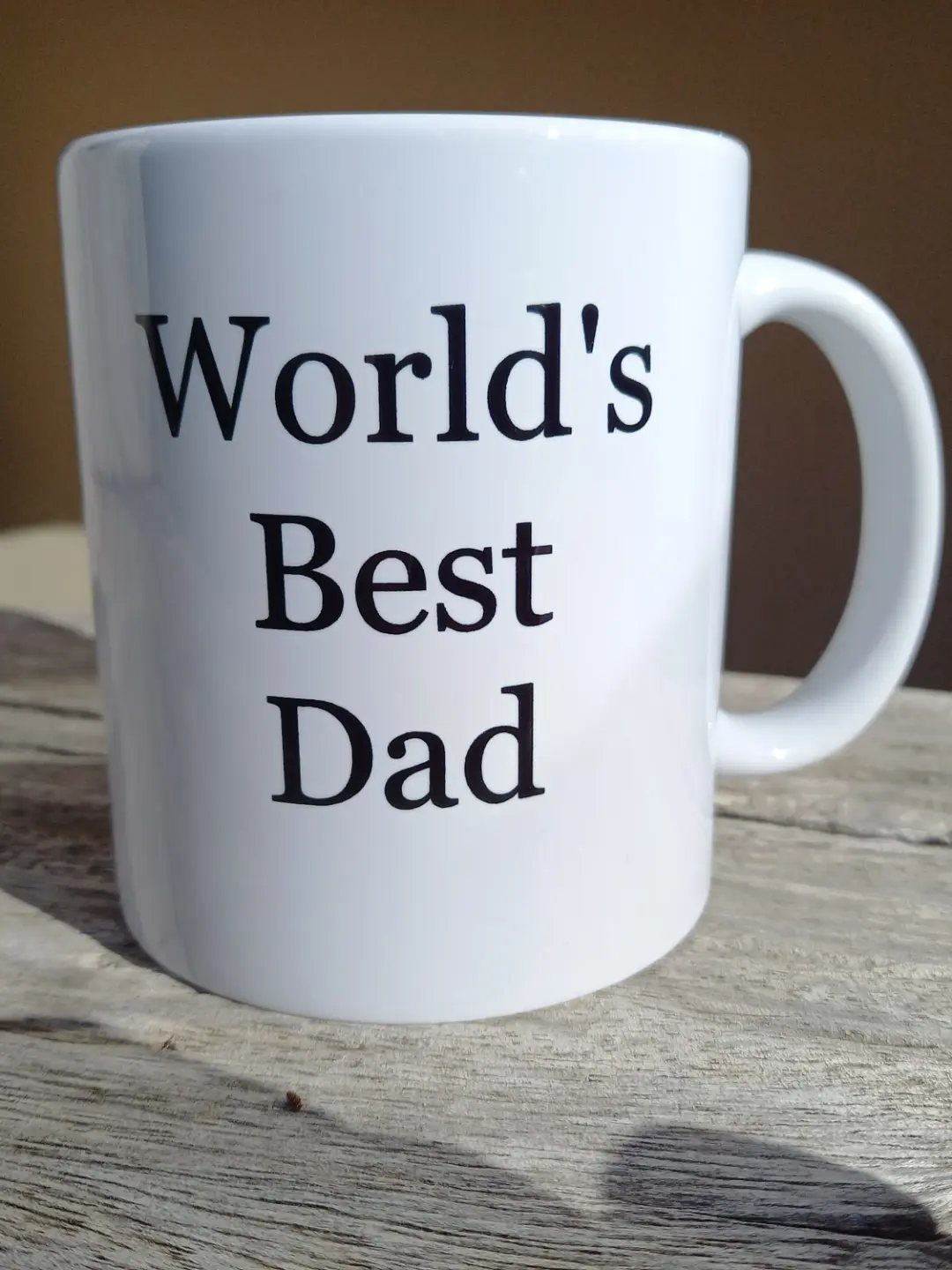 White ceramic mug with World's Best Dad text on a wooden surface