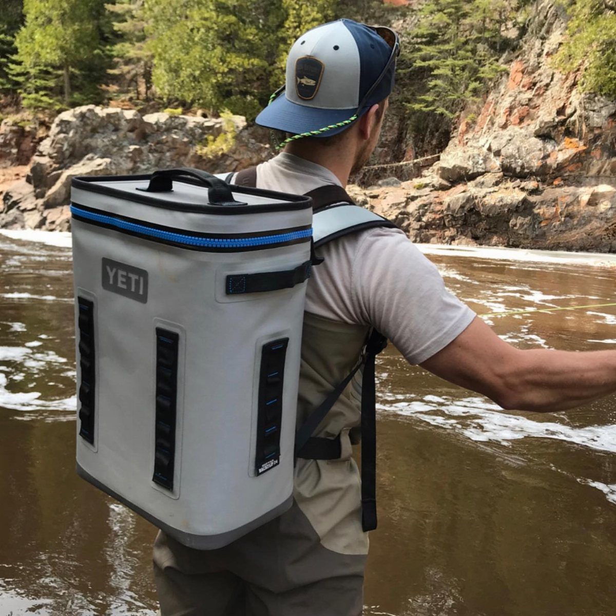 Man wearing a white YETI backpack cooler while standing in a rocky river.