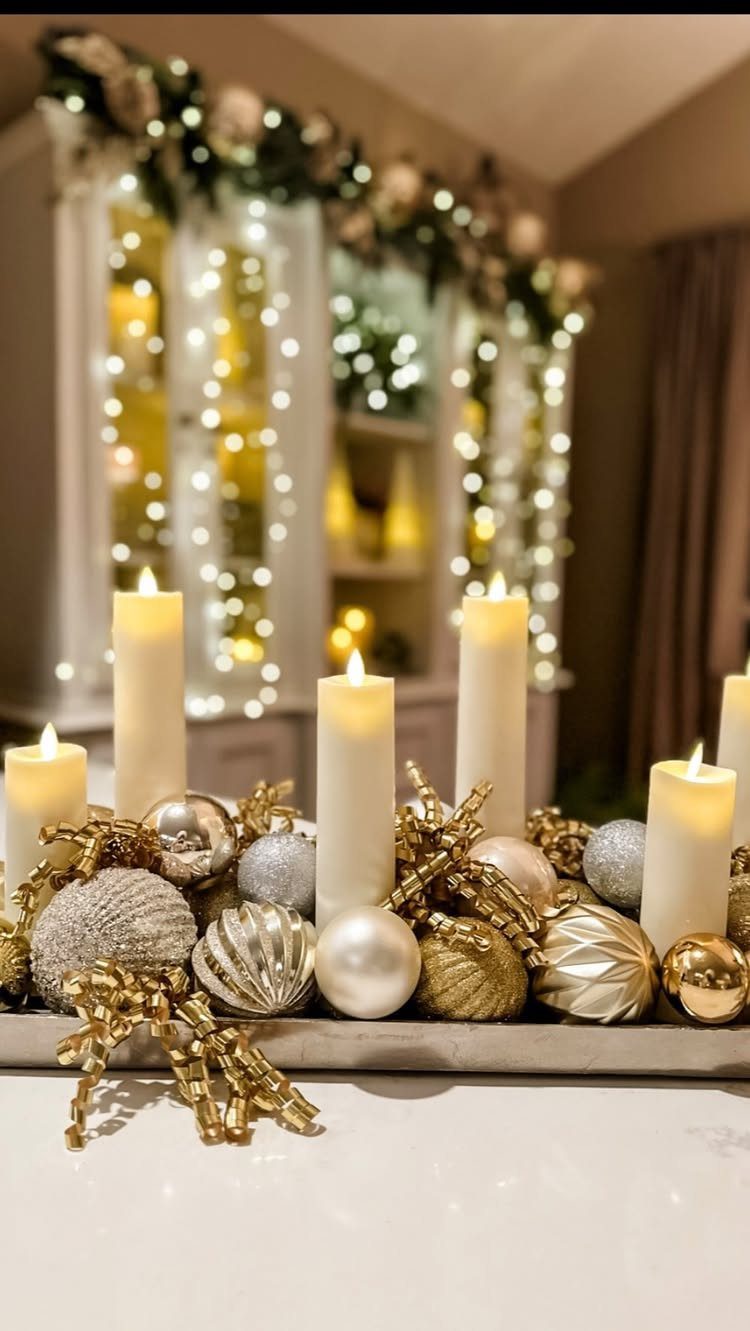 Gold and silver Christmas ornaments arranged on a tray with lit pillar candles.