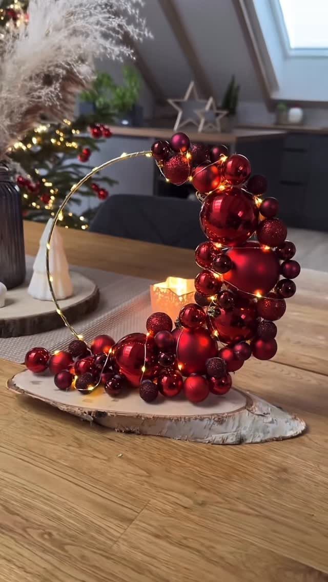 Red Christmas ornaments arranged in a crescent moon shape with fairy lights on wood.