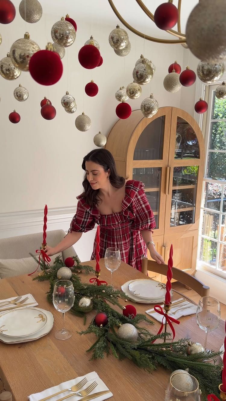 Woman standing by a dining table featuring a pine garland with red ornaments.