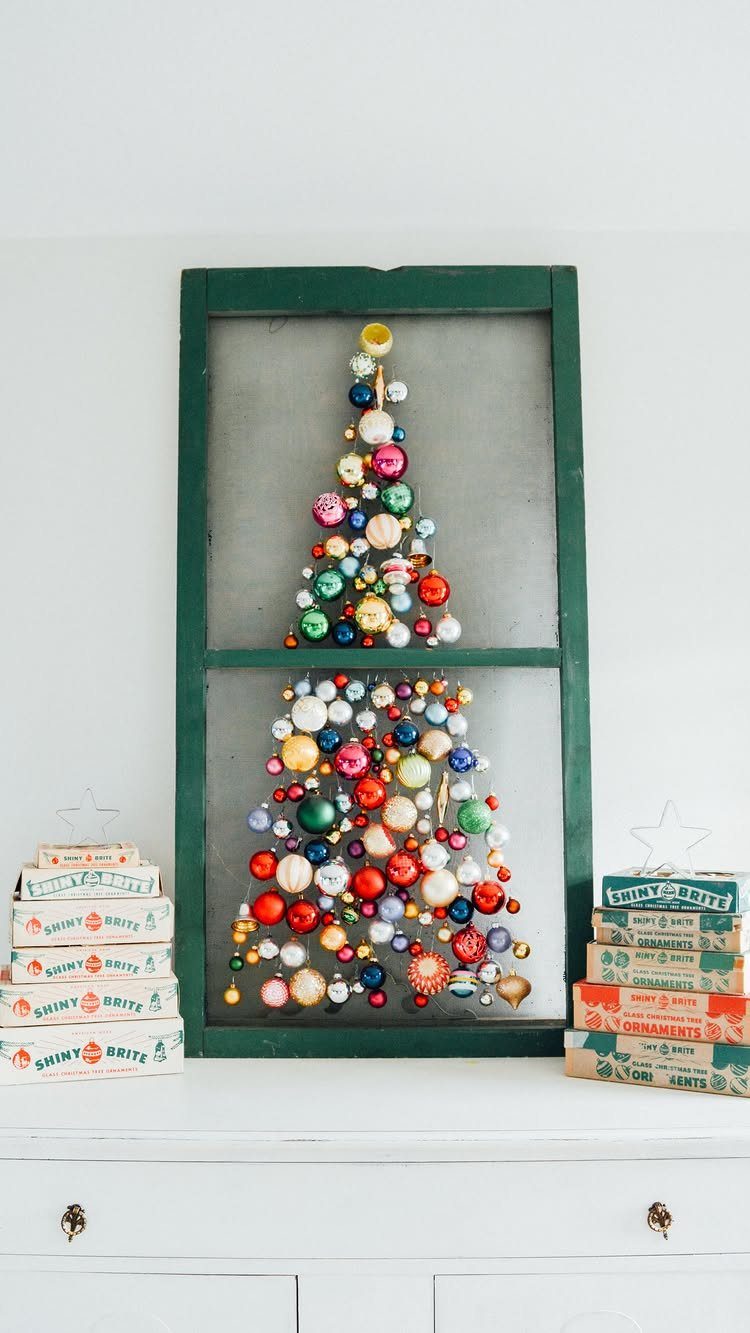 Colorful Christmas ornaments arranged as a tree inside a green window frame.