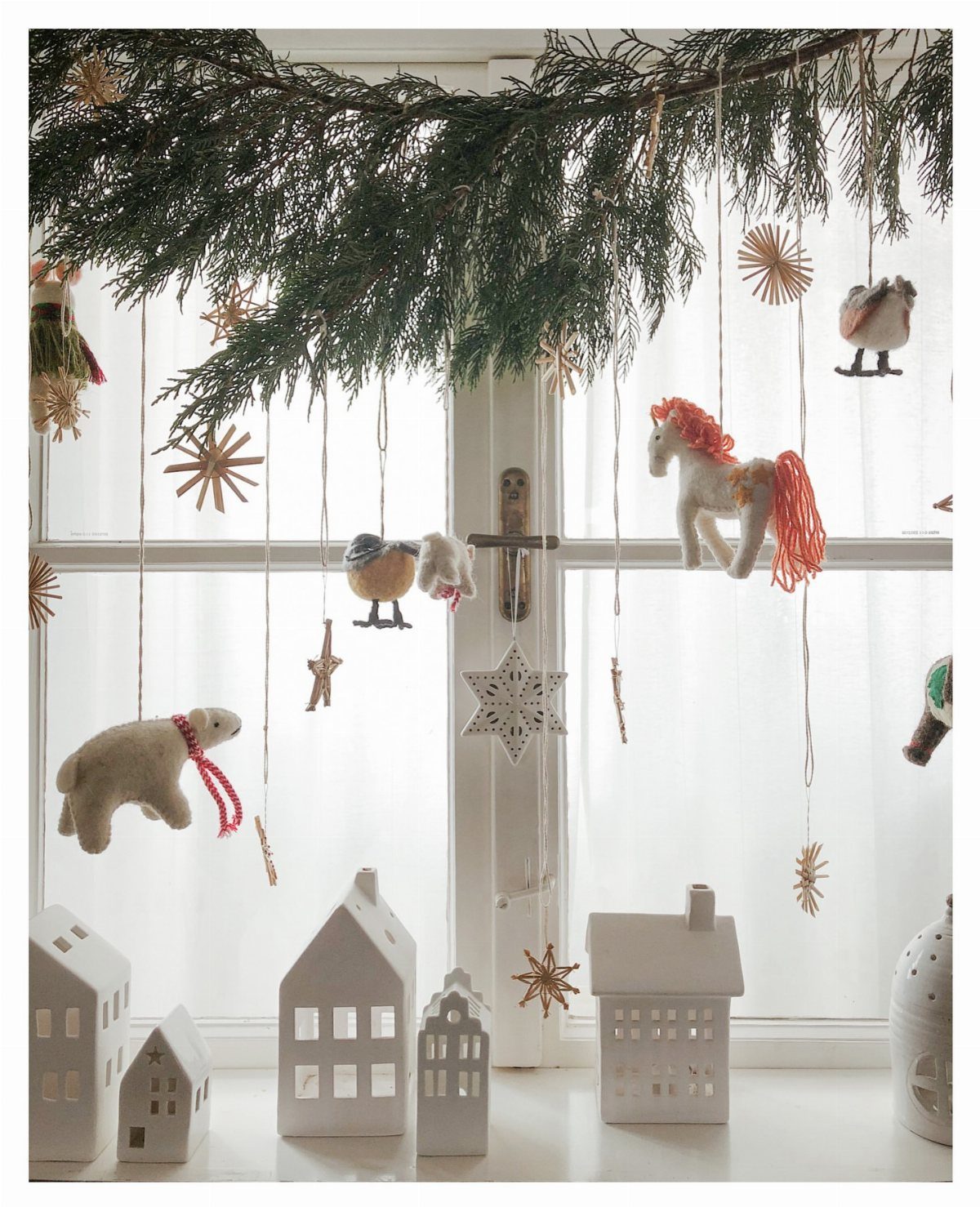 Handmade ornaments hanging from a pine garland in front of a white window