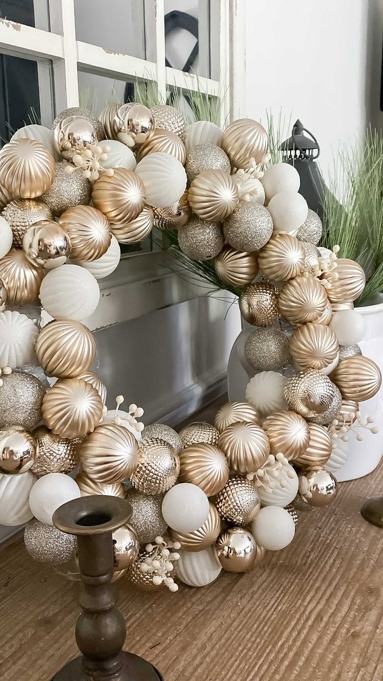 Wreath made of gold and white ornaments resting on a wooden table.